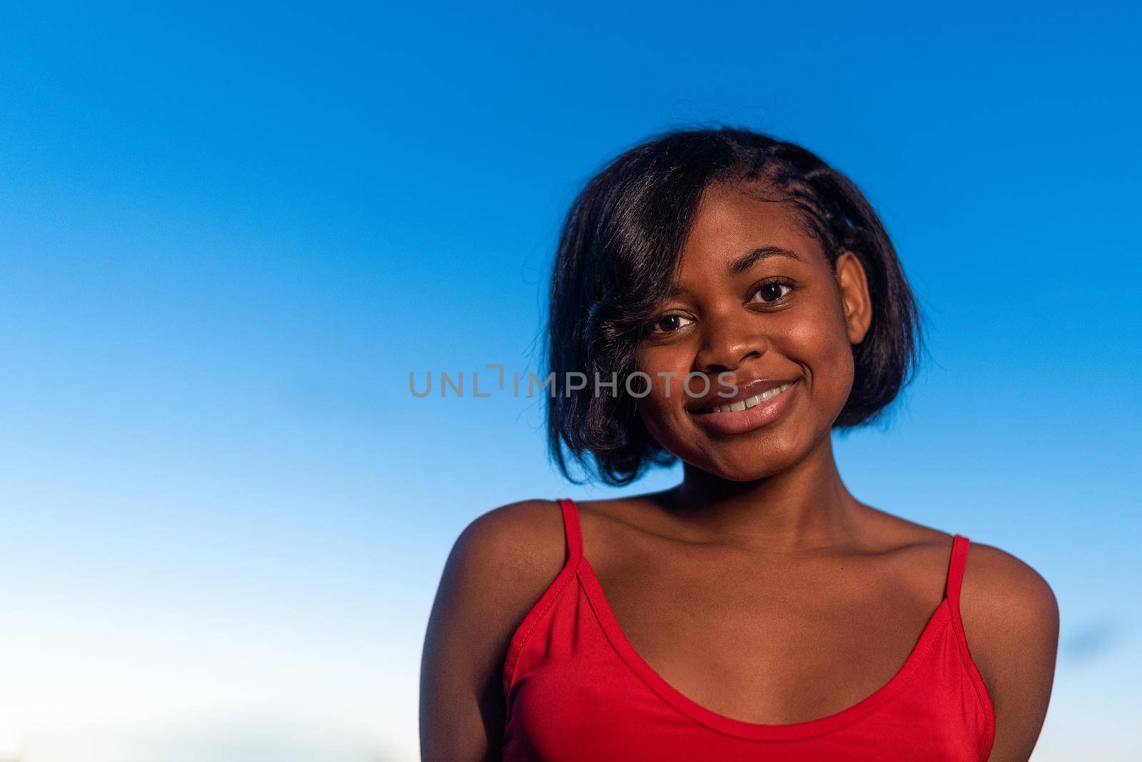 Close up portrait of a young african woman smiling while facing the camera during sunset