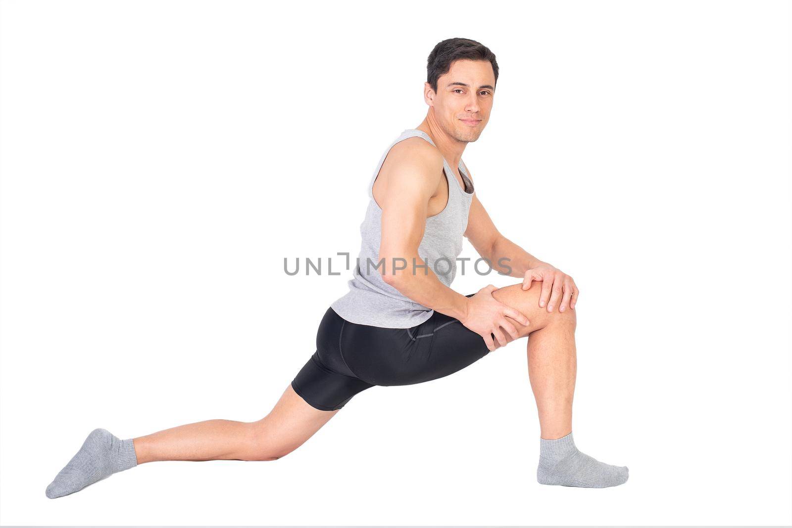 Full body of content sportsman looking at camera while stretching psoas muscle during fitness workout isolated on white background in studio