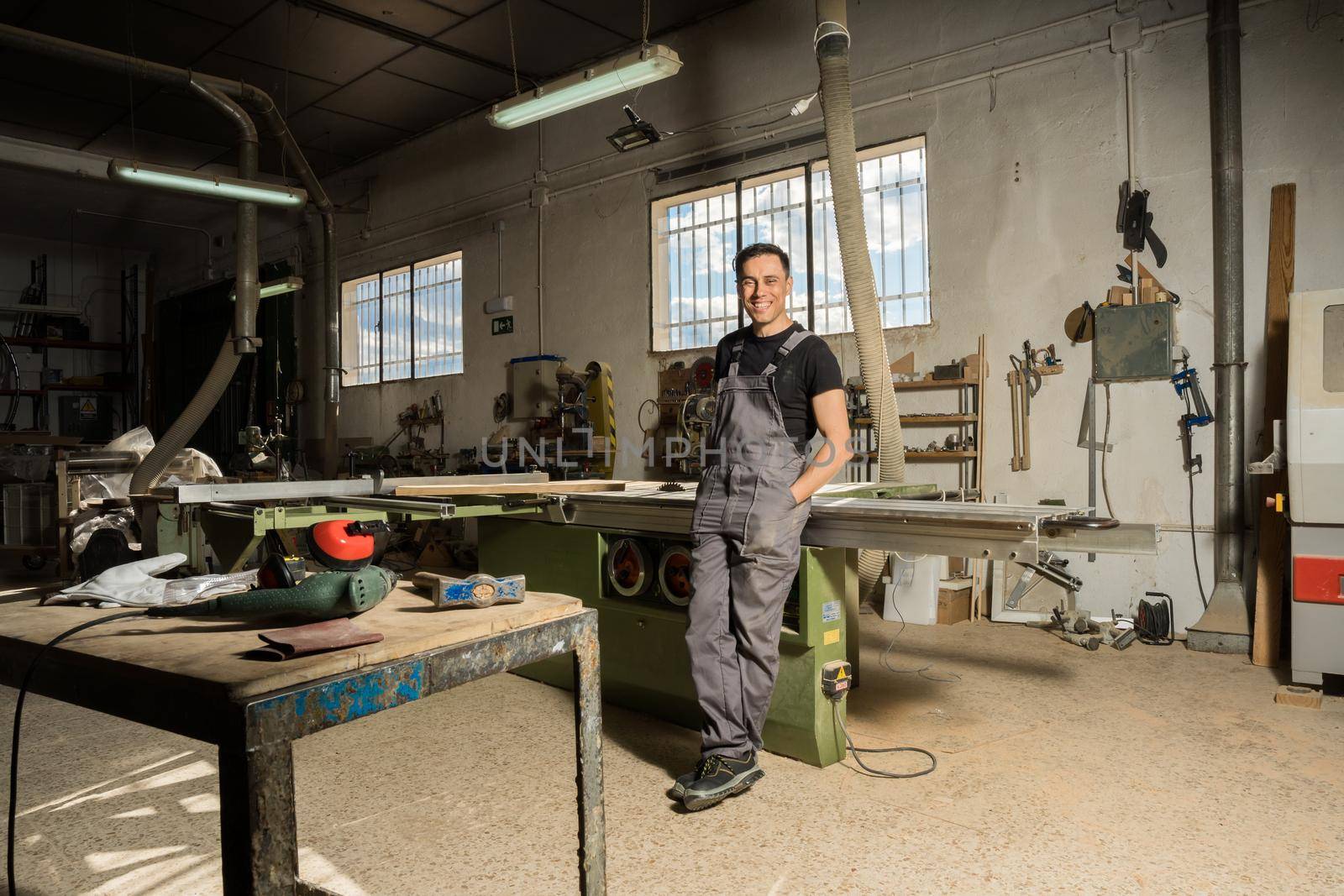 Worker standing looking at camera smiling in a factory. Long shot, full body.