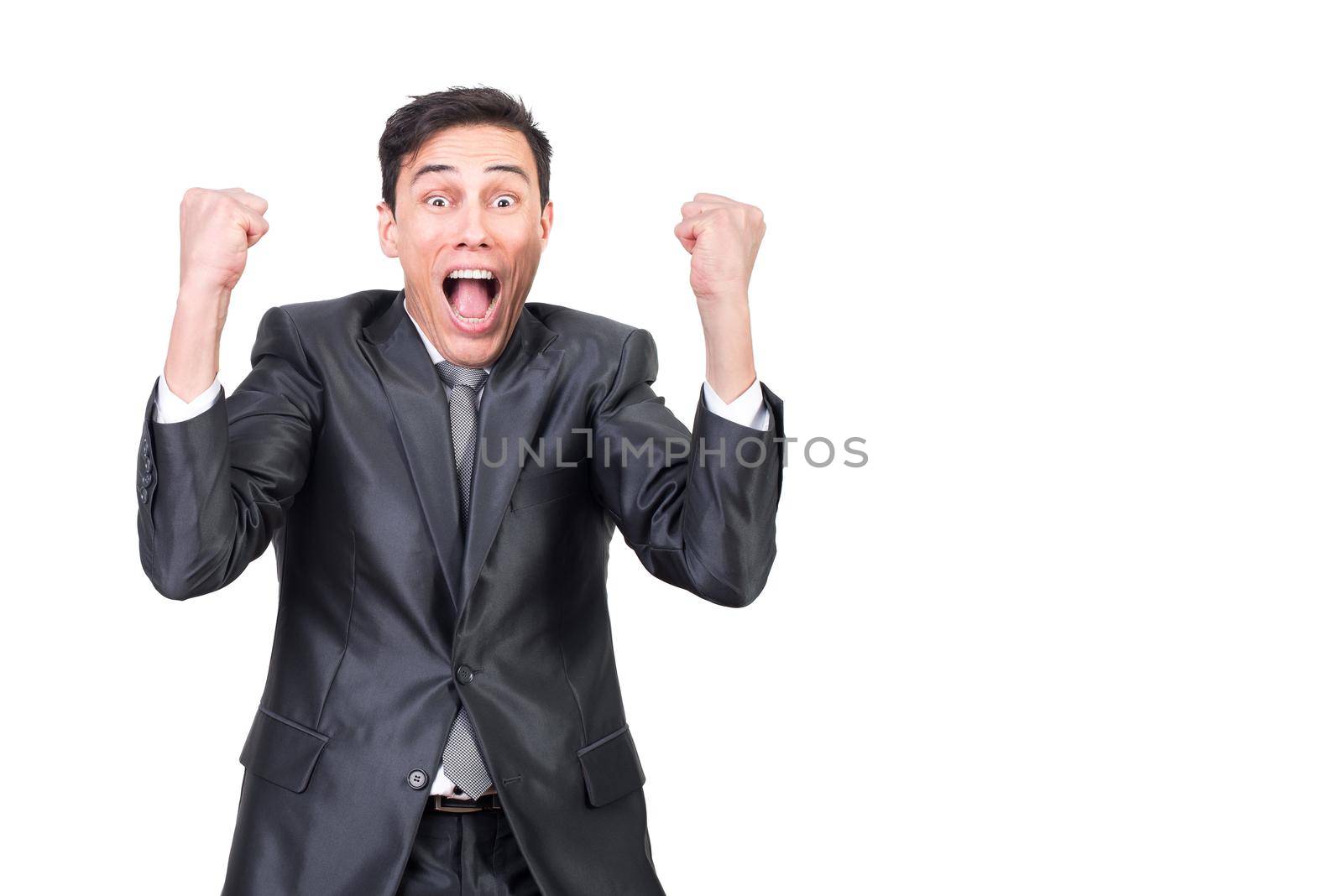 Excited young male entrepreneur in elegant suit and tie shouting loudly and clenching fists while celebrating success and looking at camera against white background