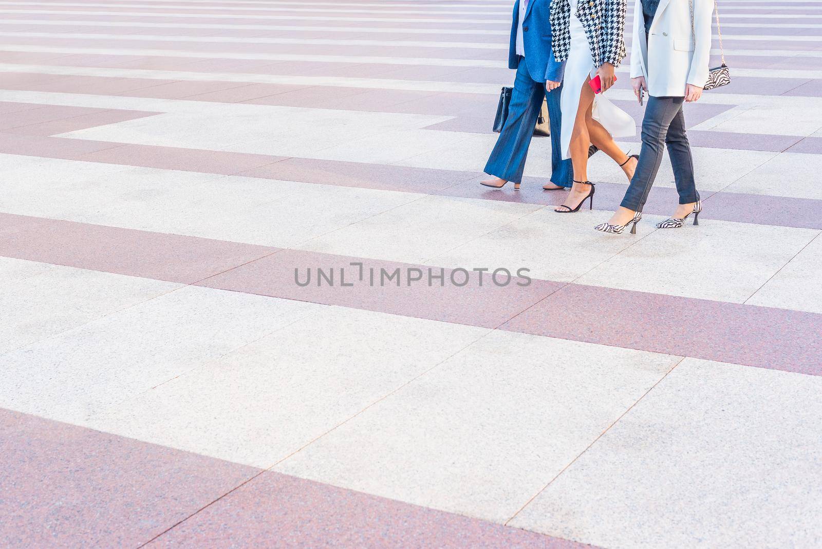 three business women walking across a pedestrian crossing. View of the legs