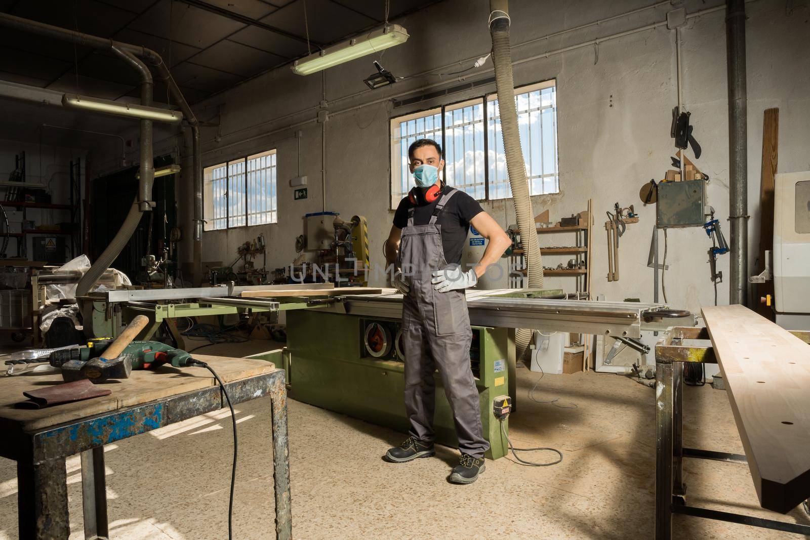 Worker standing wearing mask and protective gear looking at camera in a factory. Long shot, full body.