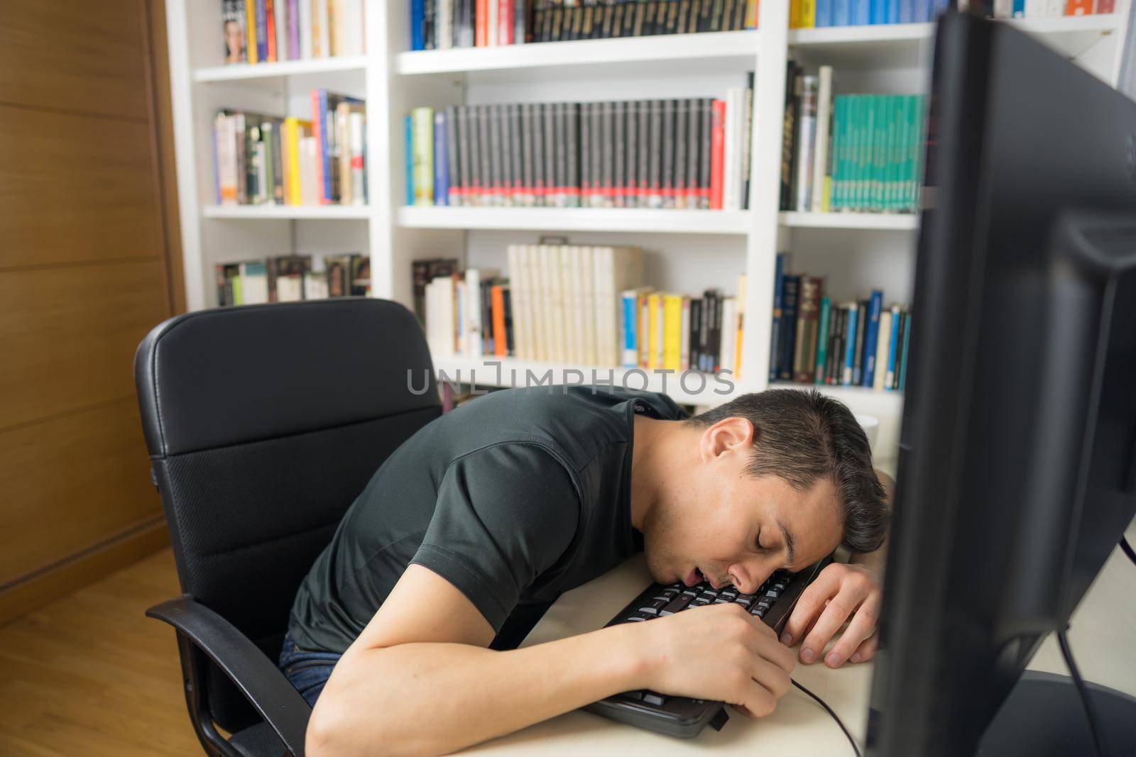 Seated man in black shirt asleep on the computer keyboard. Mid shot.