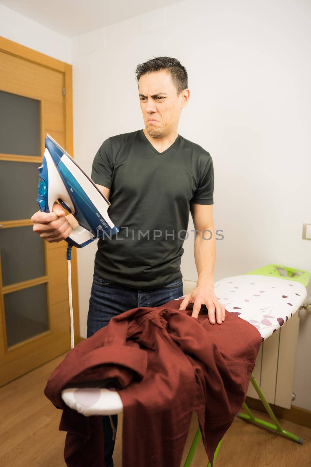 Man who does not know how to iron clothes, trying unsuccessfully to iron a shirt at home. Mid shot.