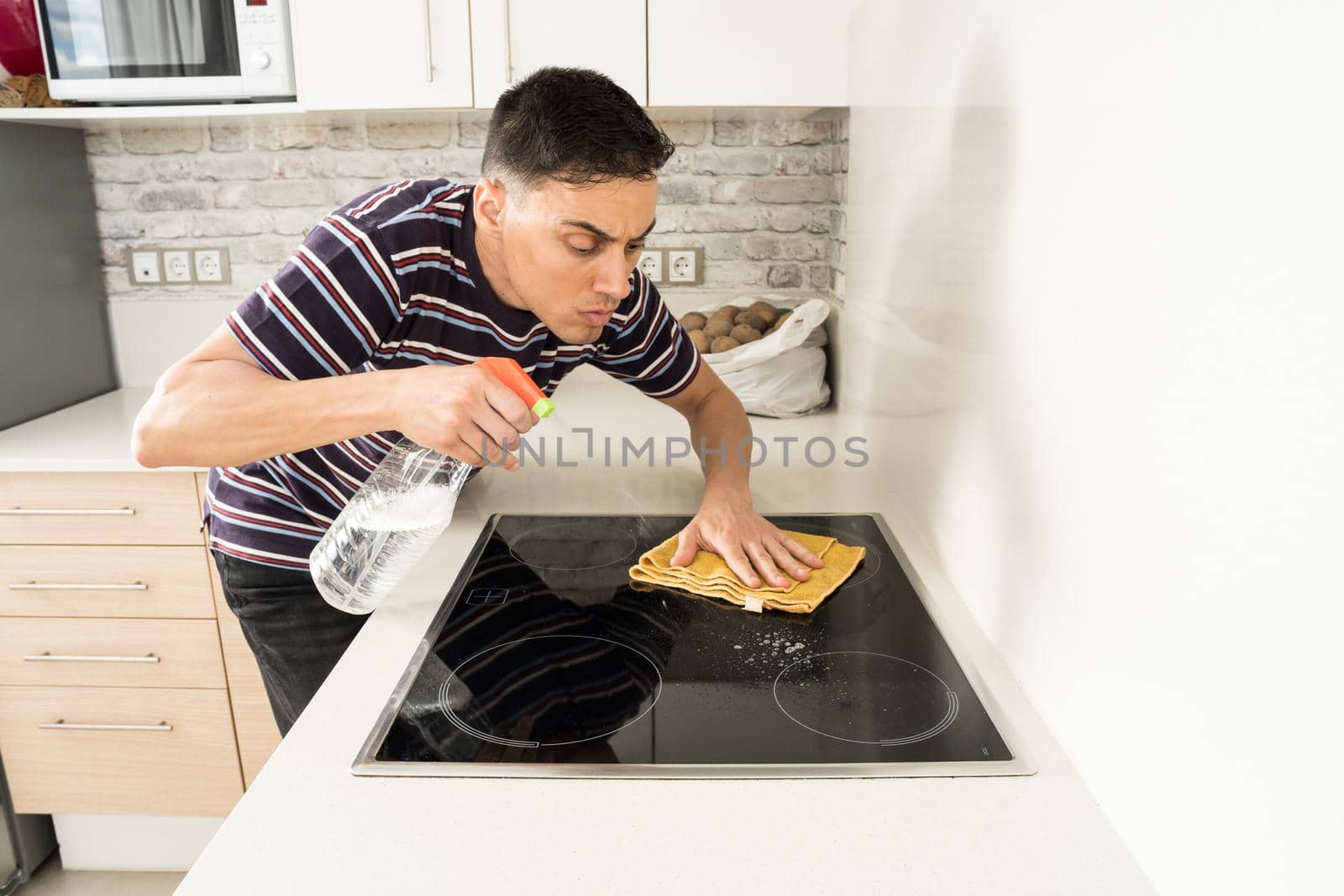 Man in casual clothes cleaning the induction hob in the kitchen with a cloth. Mid shot.
