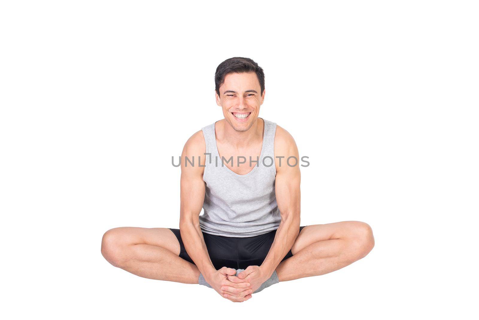 Happy sportive man in sportswear looking at camera with smile while stretching adductors muscles isolated on white background in studio