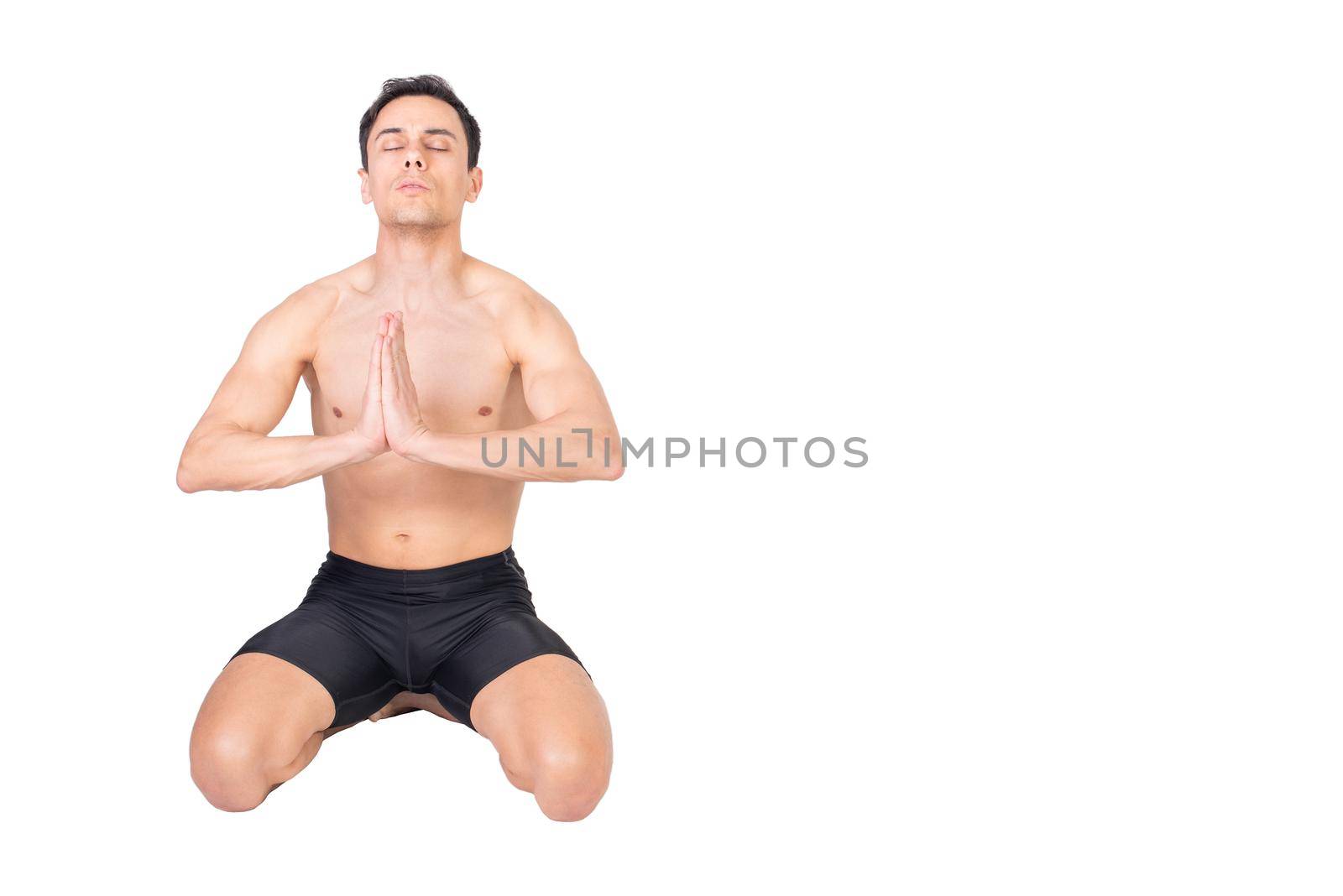 Full body of peaceful muscular male with naked torso sitting isolated on white background with closed eyes and namaste gesture