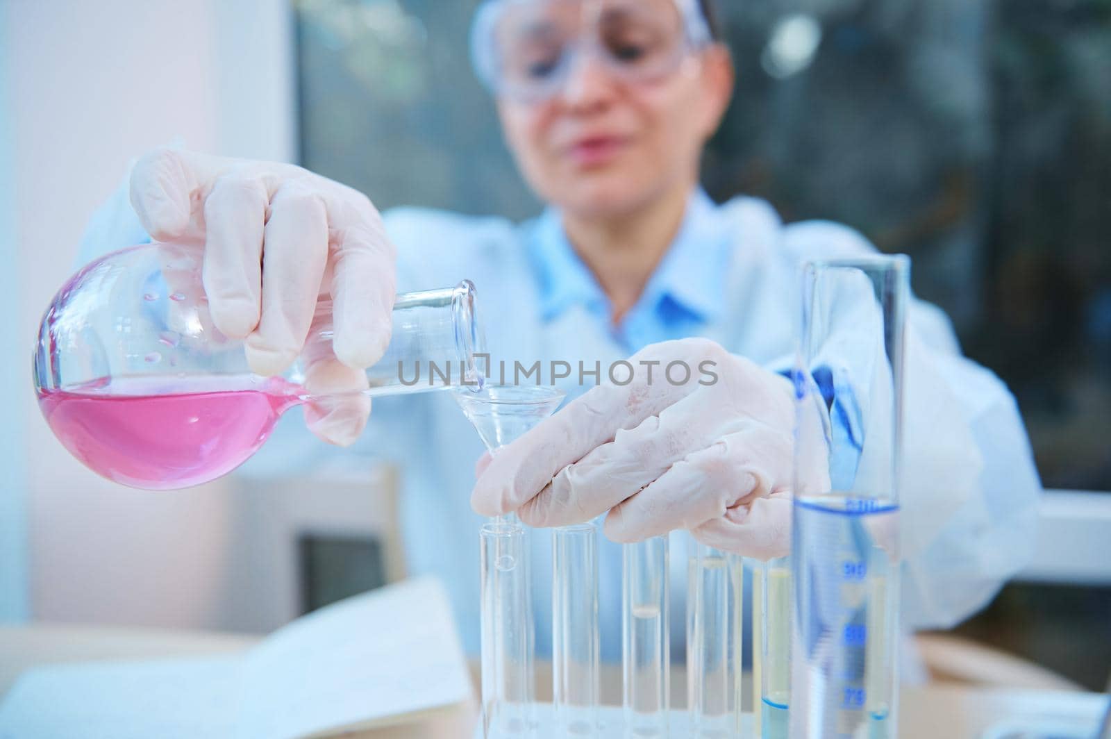 Close-up. Hands of a scientific researcher pouring liquid through a funnel from a glass laboratory flask into test tubes while making investigations and clinical researche in medicine and pharmacology