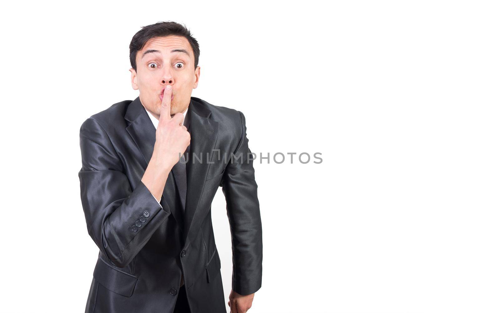 Quiet man in elegant suit covering mouth with finger and looking at camera while keeping silence isolated on white background
