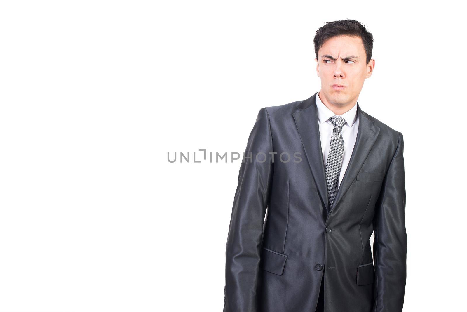 Distrustful male manager in formal suit standing against white background and looking away with puzzled look