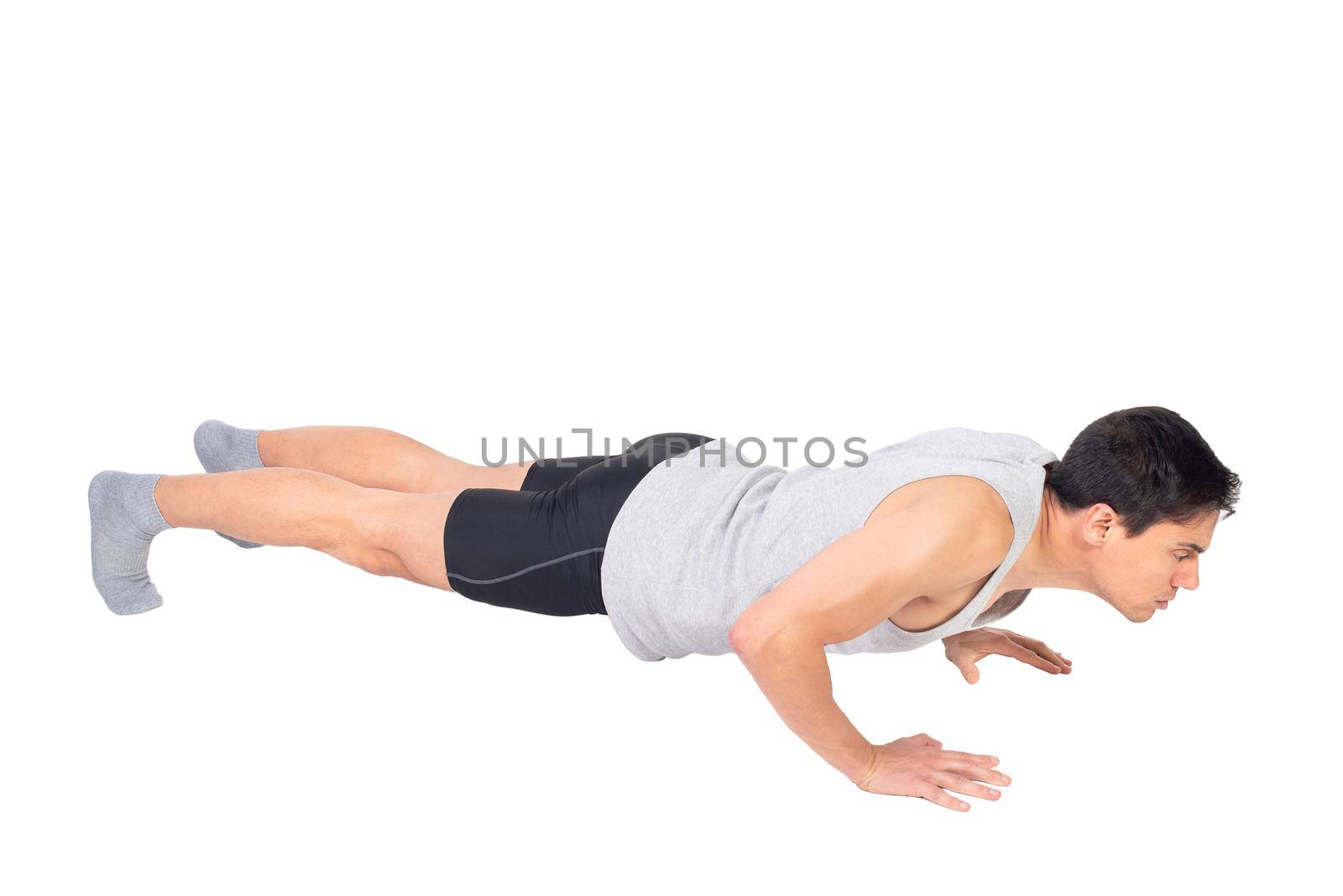 Full body side view of sportive male lowering body to ground while doing push ups exercise during fitness training isolated on white background