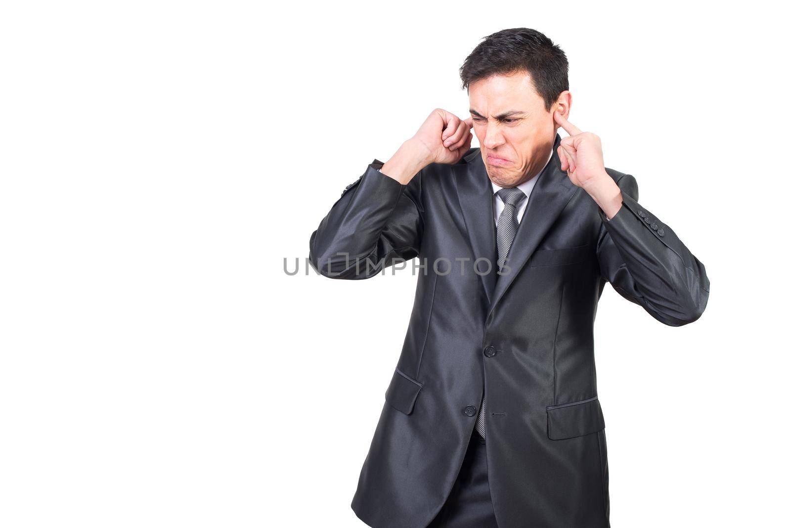 Frustrated young male manager in classy suit covering ears with fingers while standing on white background
