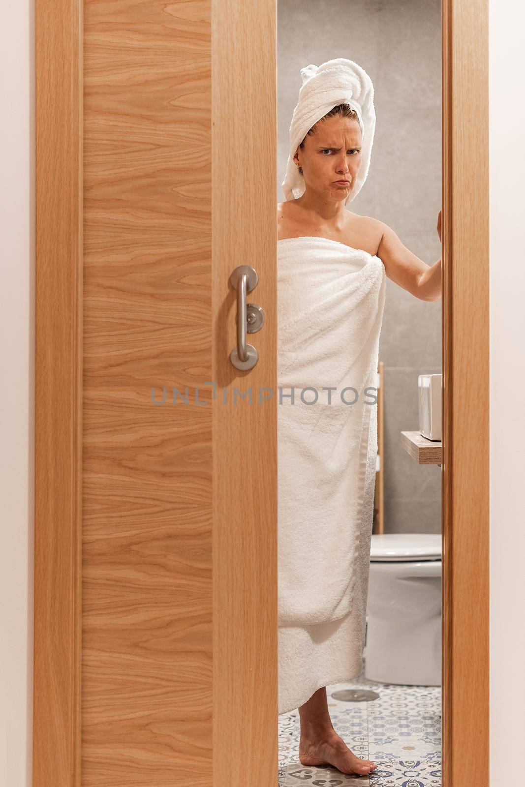 Adult woman wrapped with towels annoyed at being spied on closes bathroom door. Concept of hotel.