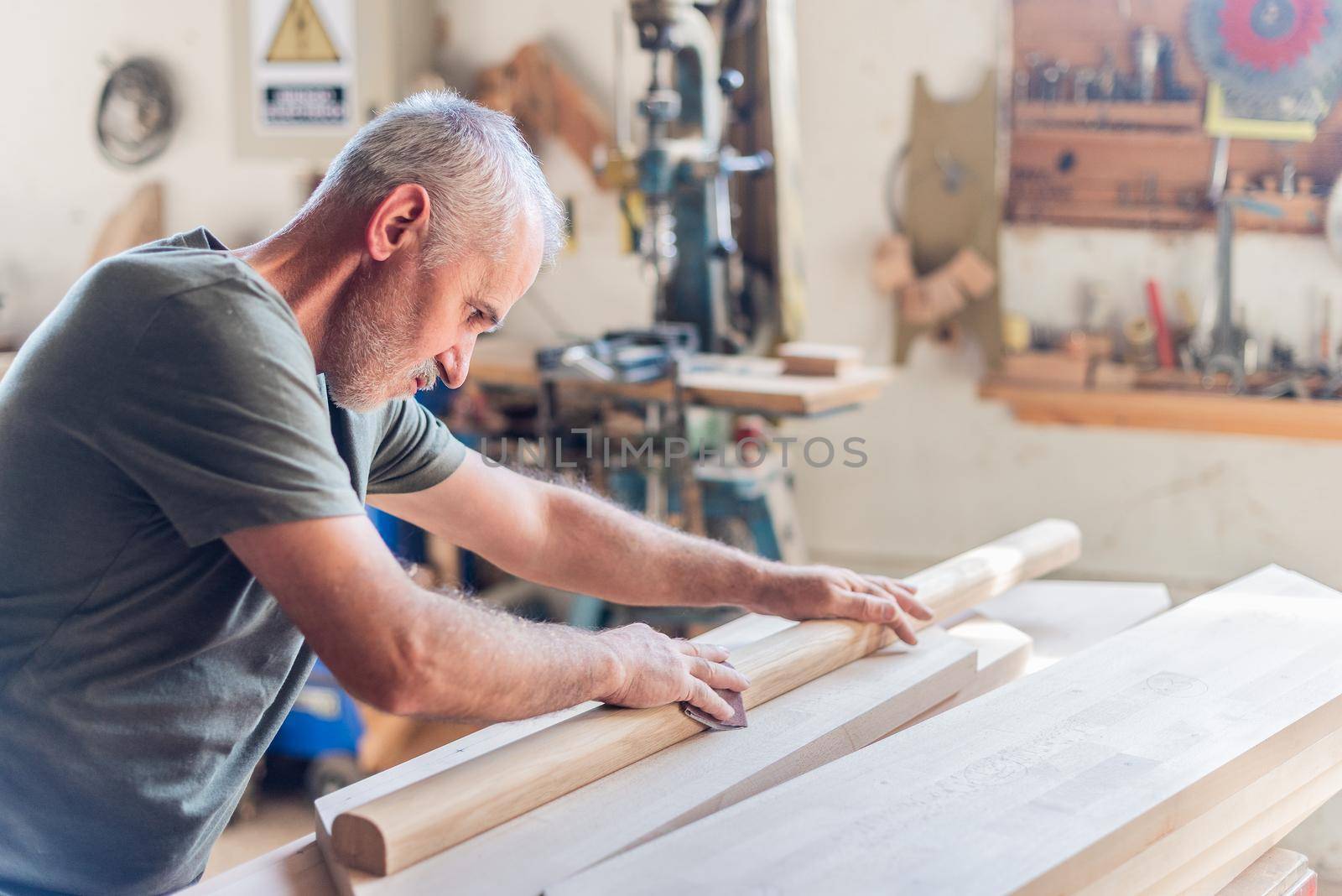 Standing senior man sanding wood with his arms, blurred horizontal background