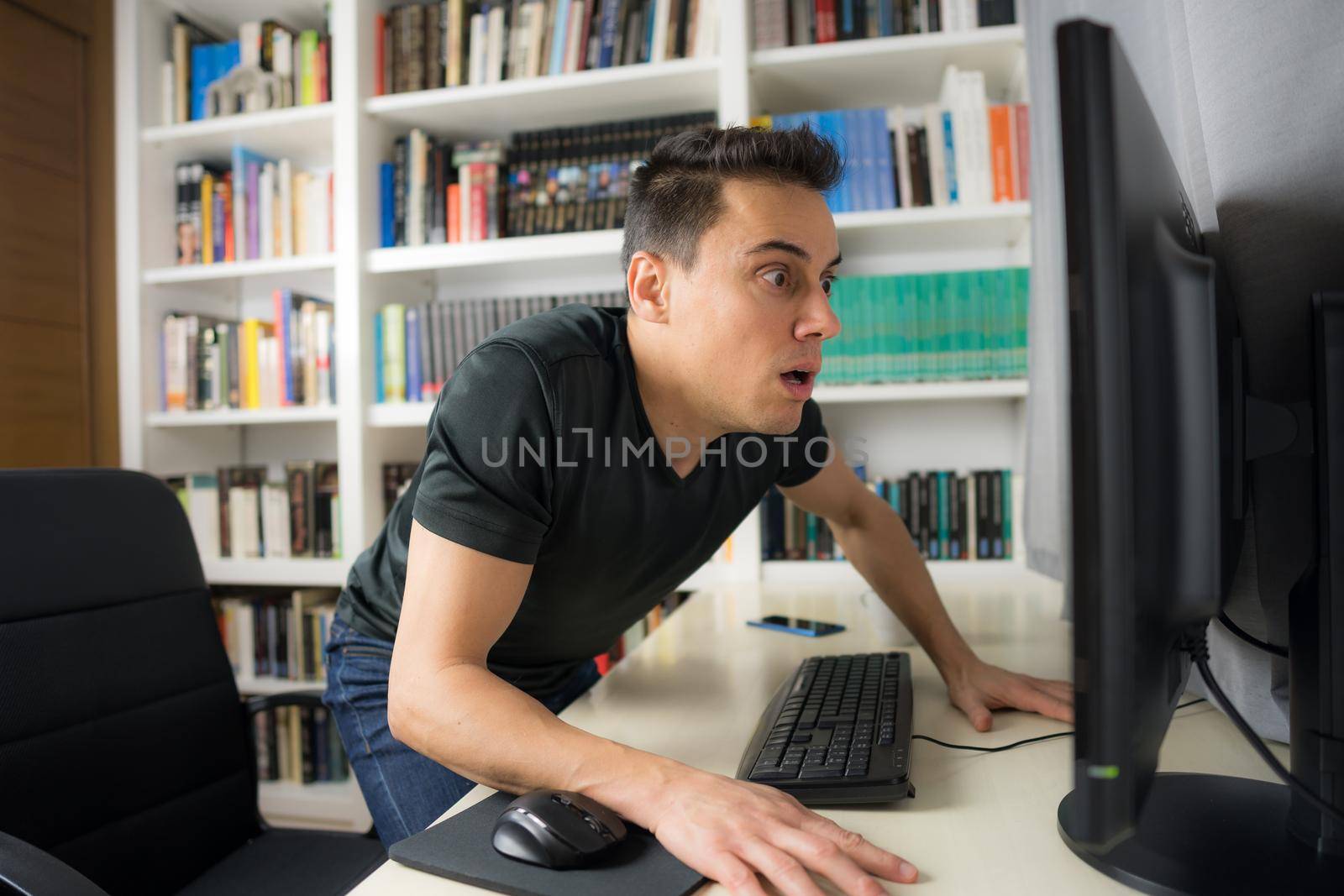 Seated man in black shirt looking at the computer screen very surprised. Mid shot.