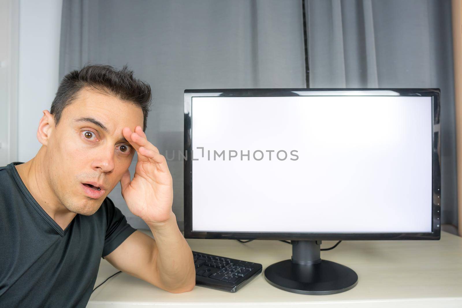 Surprised man in black shirt pointing at a computer screen announcing important news. Close up.