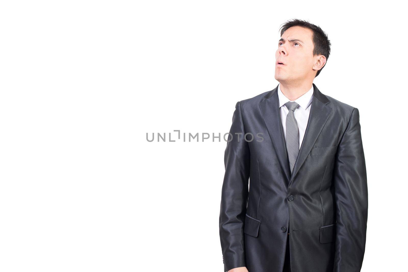 Mid shot of doubting male in elegant suit looking up with puzzled face while standing isolated on white background in studio