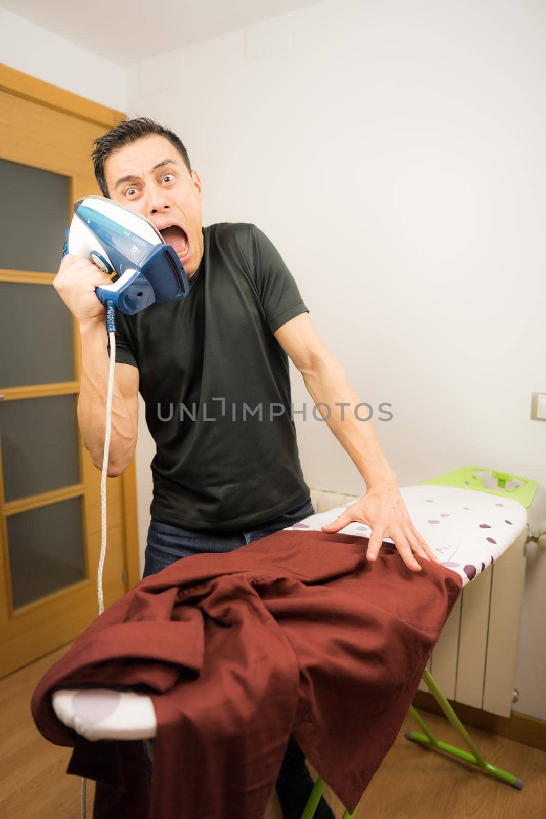 Man who does not know how to iron clothes, trying unsuccessfully to iron a shirt at home. Mid shot.