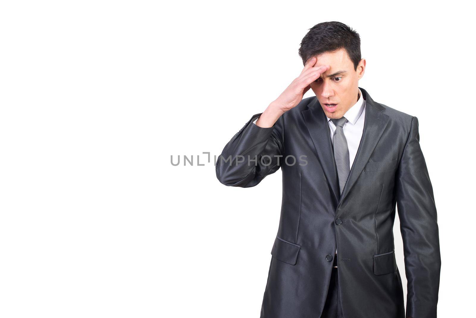 Shocked male entrepreneur in elegant suit looking down with hand on forehead while standing isolated on white background in studio