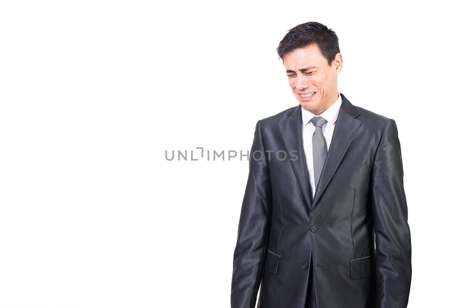Dissatisfied male entrepreneur with black hair in formal suit crying with closed eyes while standing isolated on white background in studio