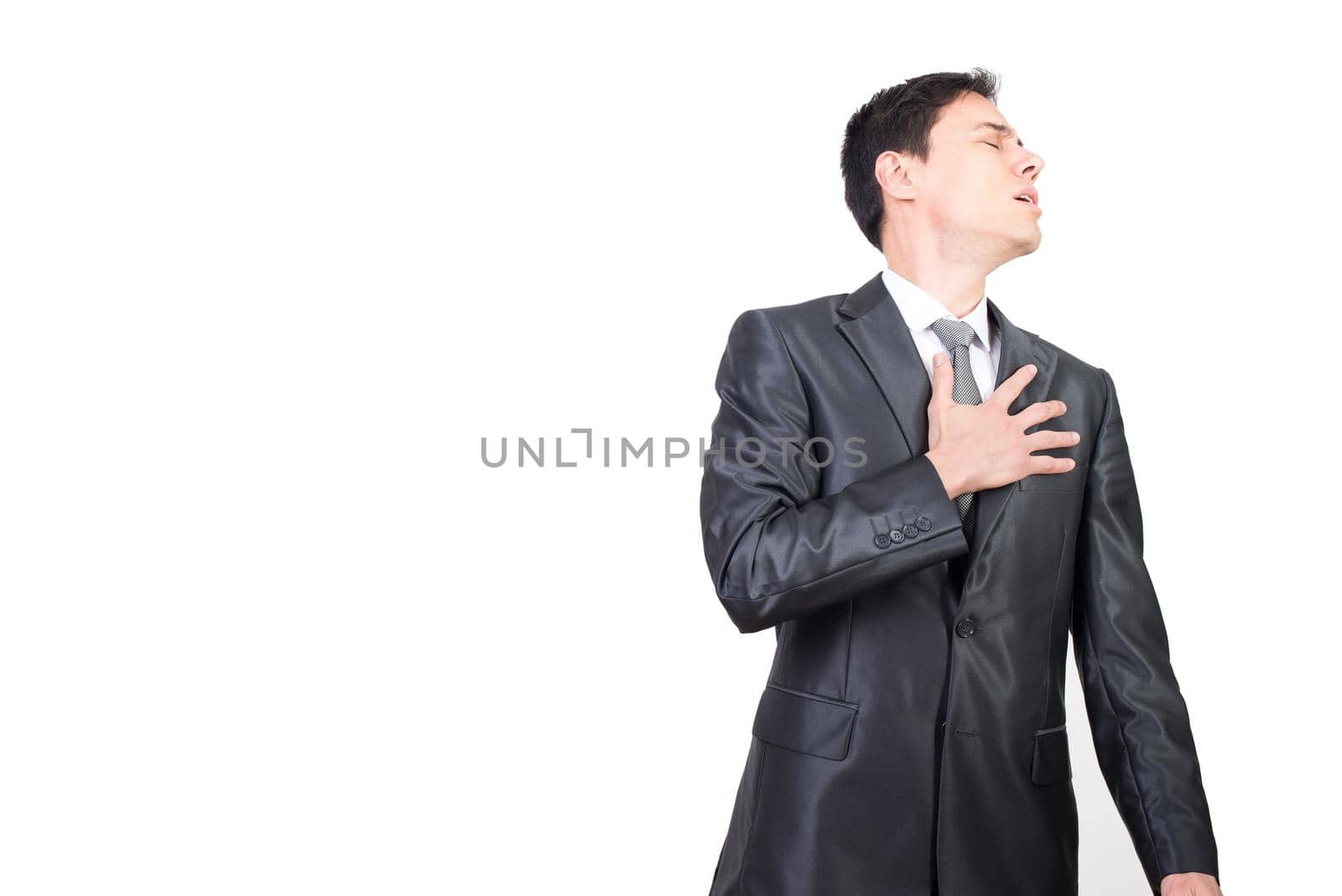 Unpleasant male in elegant wear with closed eyes touching chest with hand while suffering isolated on white background in light studio