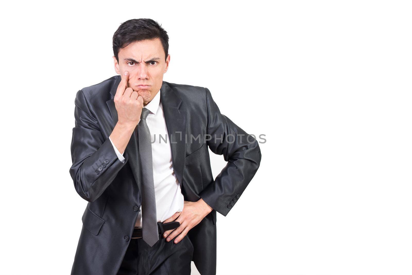 Serious man in formal suit pointing at eye while keeping control and looking at camera with concern against white background