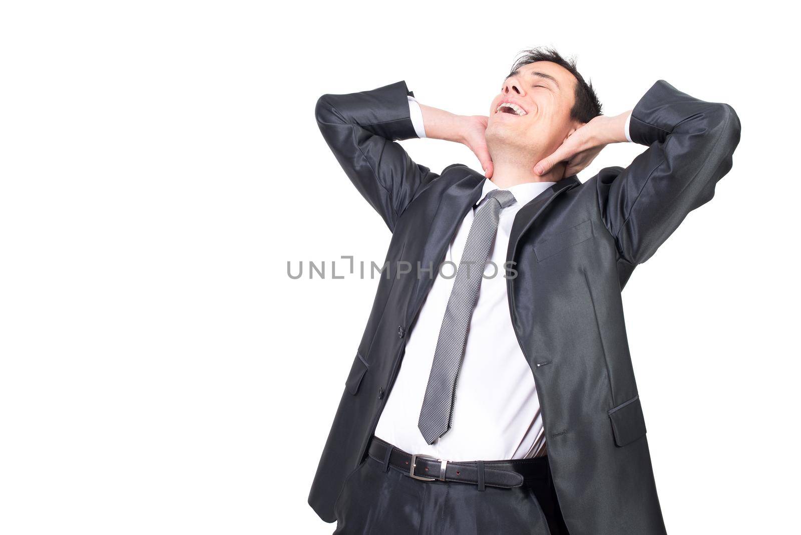 Delighted relaxed male entrepreneur with closed eyes and dark hair wearing black formal suit touching neck and stretching against white background