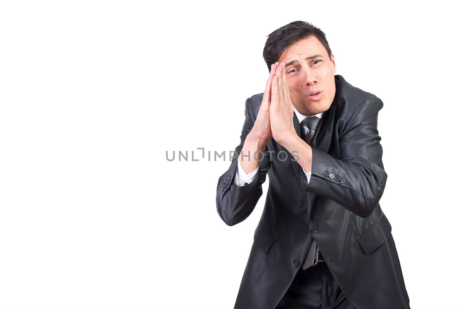 Serious adult male wearing black formal suit supplicating with clasped hands and looking at camera against white background