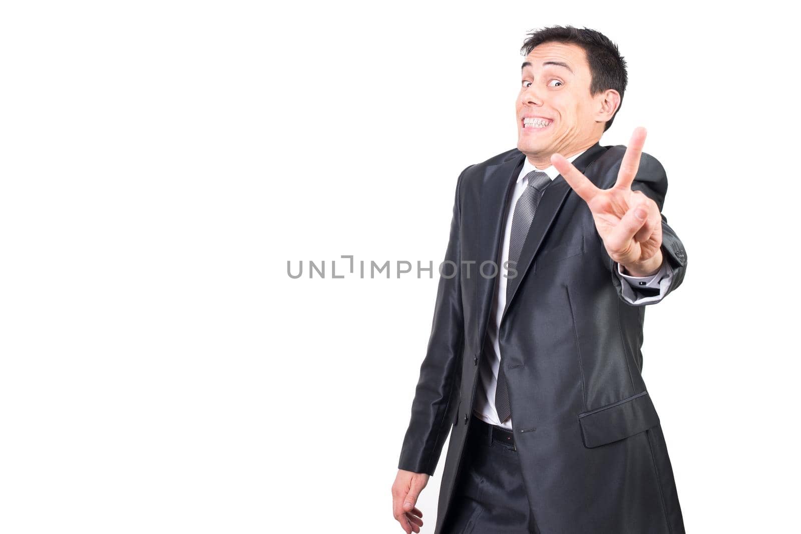 Delighted male entrepreneur in formal suit showing peace gesture and looking at camera isolated on white background in light studio