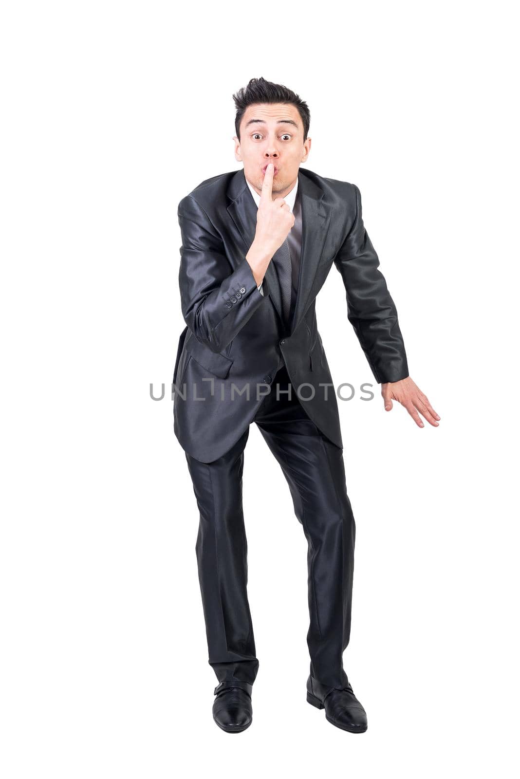 Full body of comic male entrepreneur touching lips and showing secret sign while standing against white background and looking at camera in studio