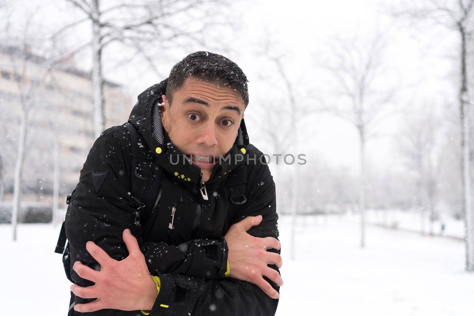 Portrait of an adult caucasian man gesturing that is cold in the snow in a urban landscape