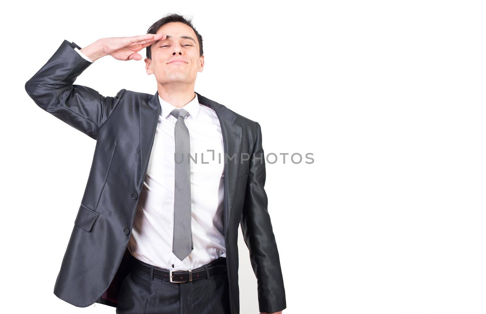 Positive soldier in elegant suit making salute gesture and looking at camera with smile isolated on white background in studio