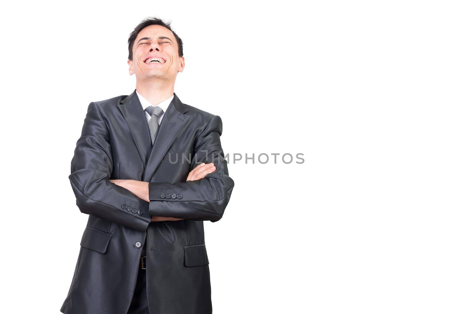 Positive male in formal suit laughing with closed eyes while standing with crossed arms isolated on white background in studio