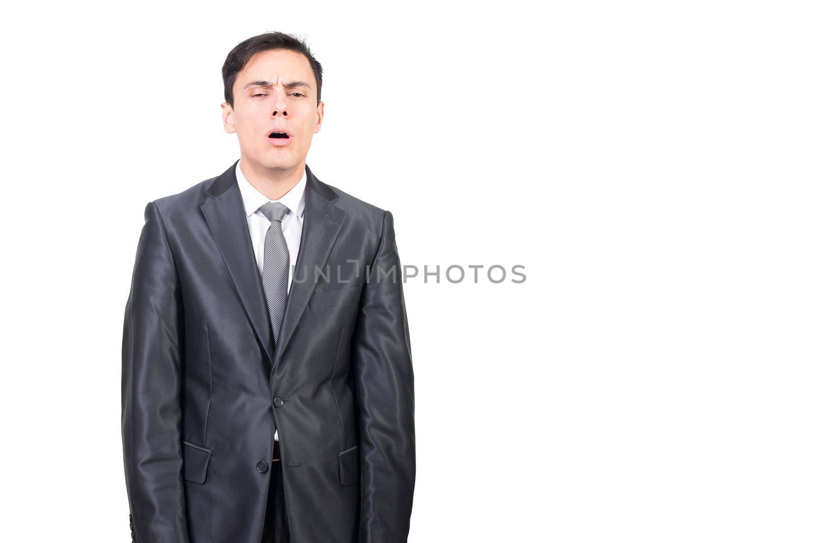 Tired man in elegant gray suit looking away with sleepy face while standing isolated on white background in light studio
