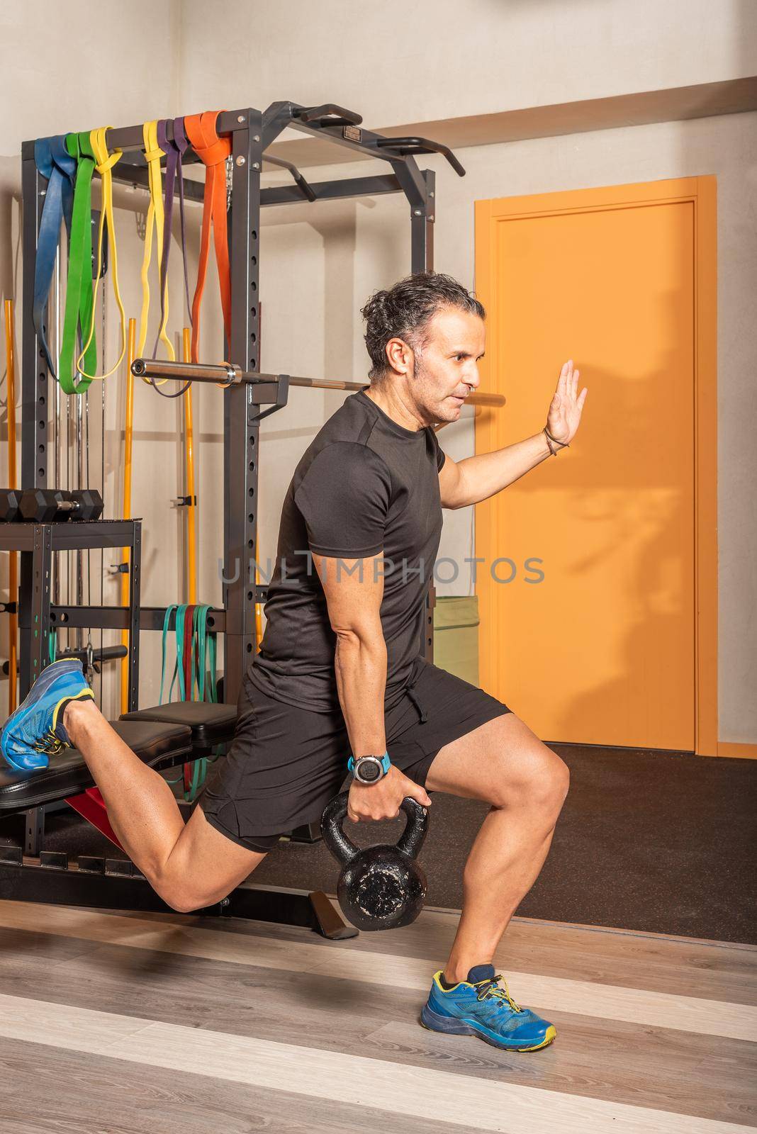 Sportsman in sportswear doing lunges with a kettlebells in her hand with one leg resting on a bench in gym. Concept of exercise with equipment in gym.