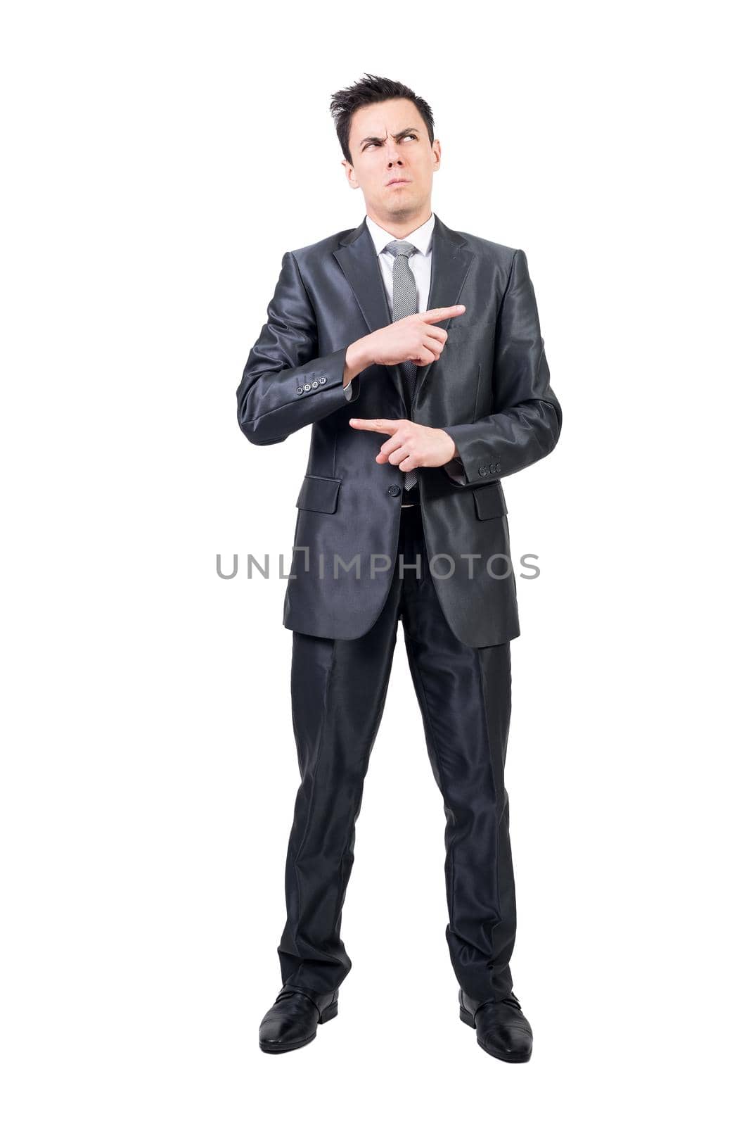 Puzzled man in formal suit pointing with fingers and looking up with serious face isolated on white background in light studio