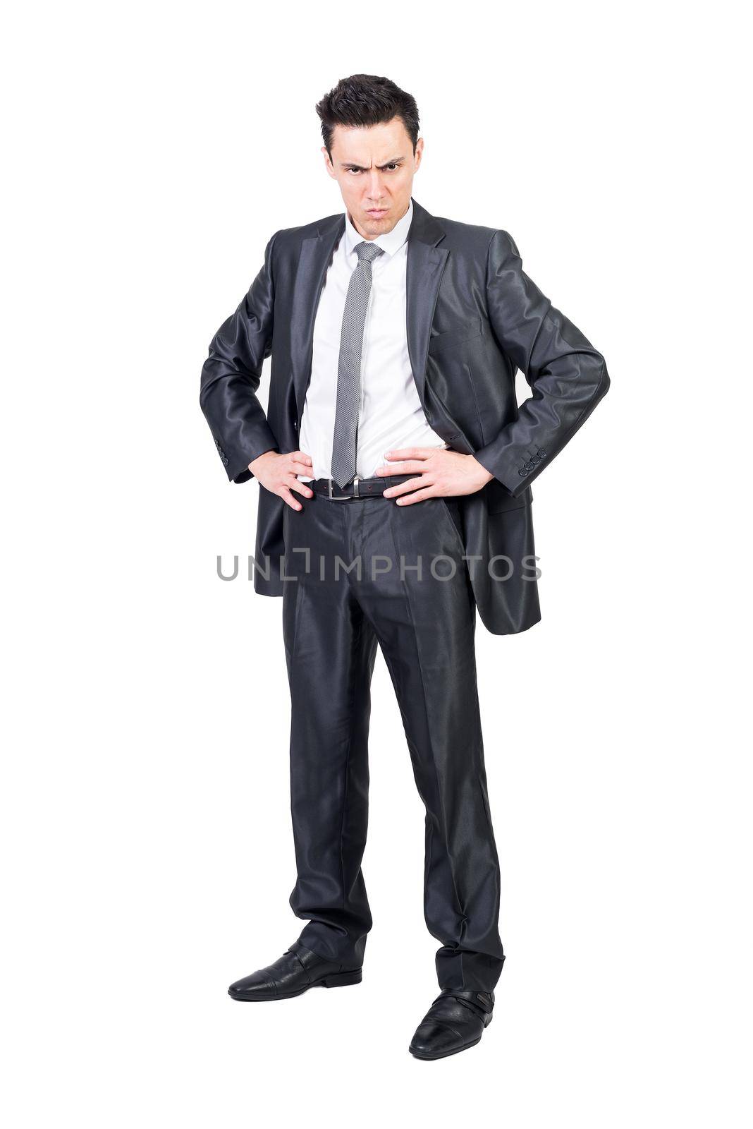 Full length of irritated male entrepreneur in formal suit standing with hands on waist and looking at camera with anger on white background