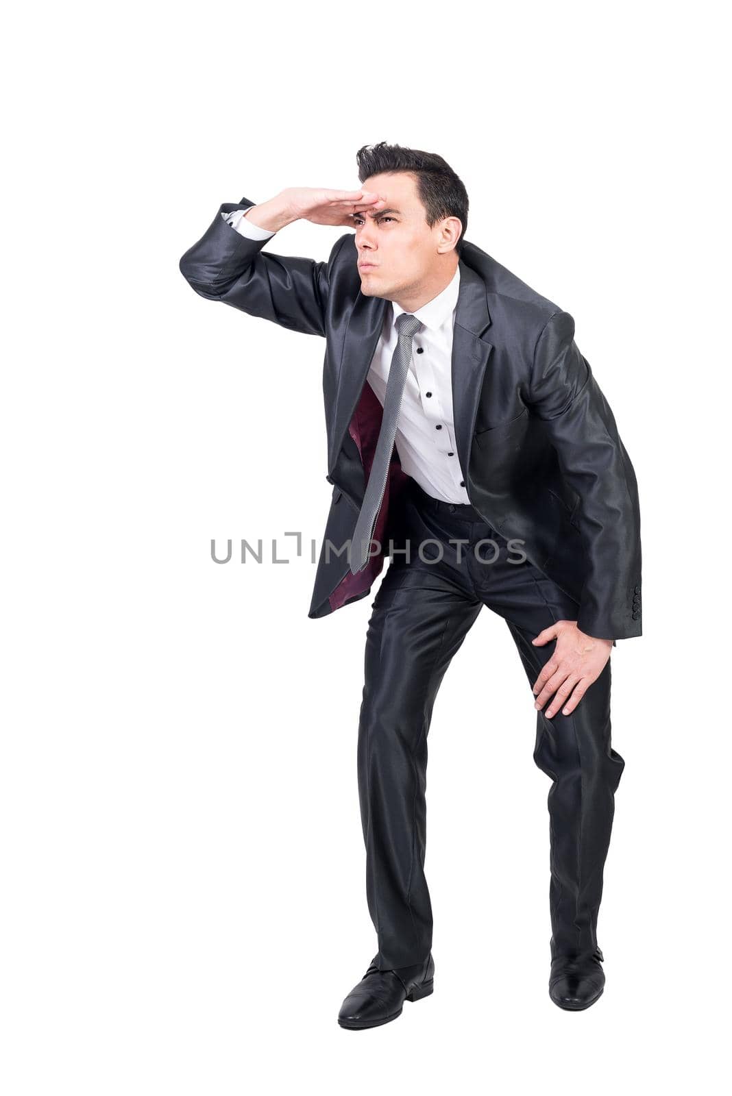 Full body of focused male in elegant suit looking away while observing with hand on forehead isolated on white background in studio