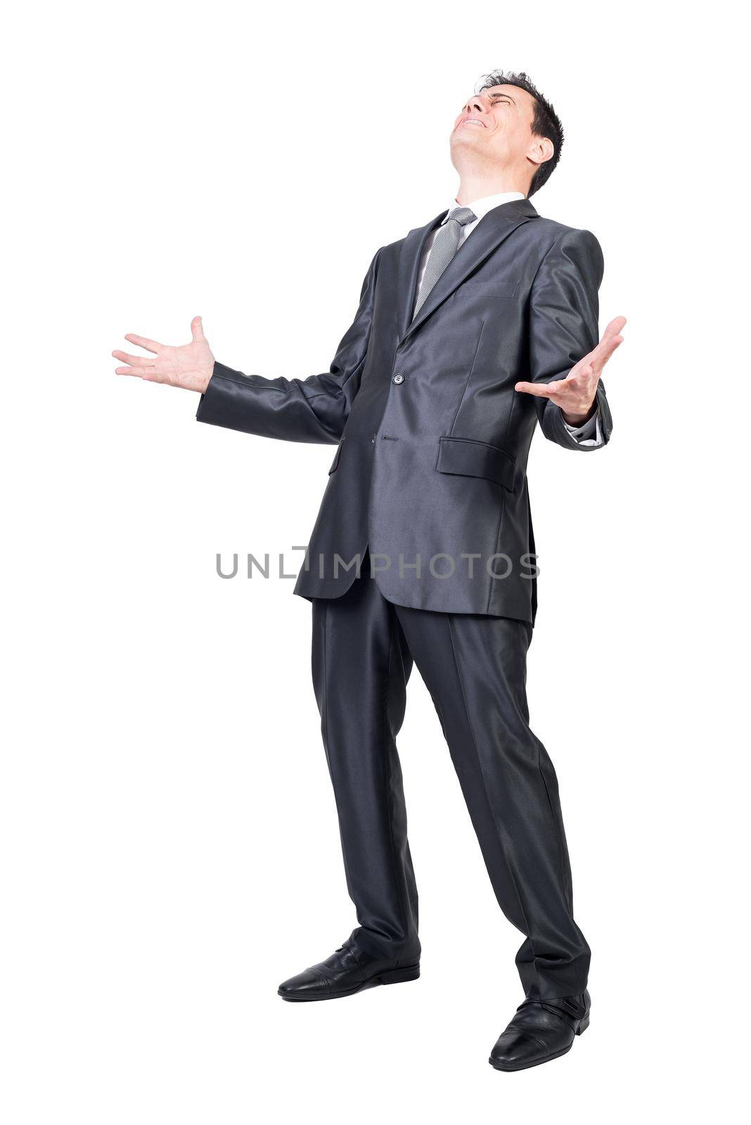 Full length of sad suffering man in elegant suit with dark hair standing in white studio with hands apart and closed eyes