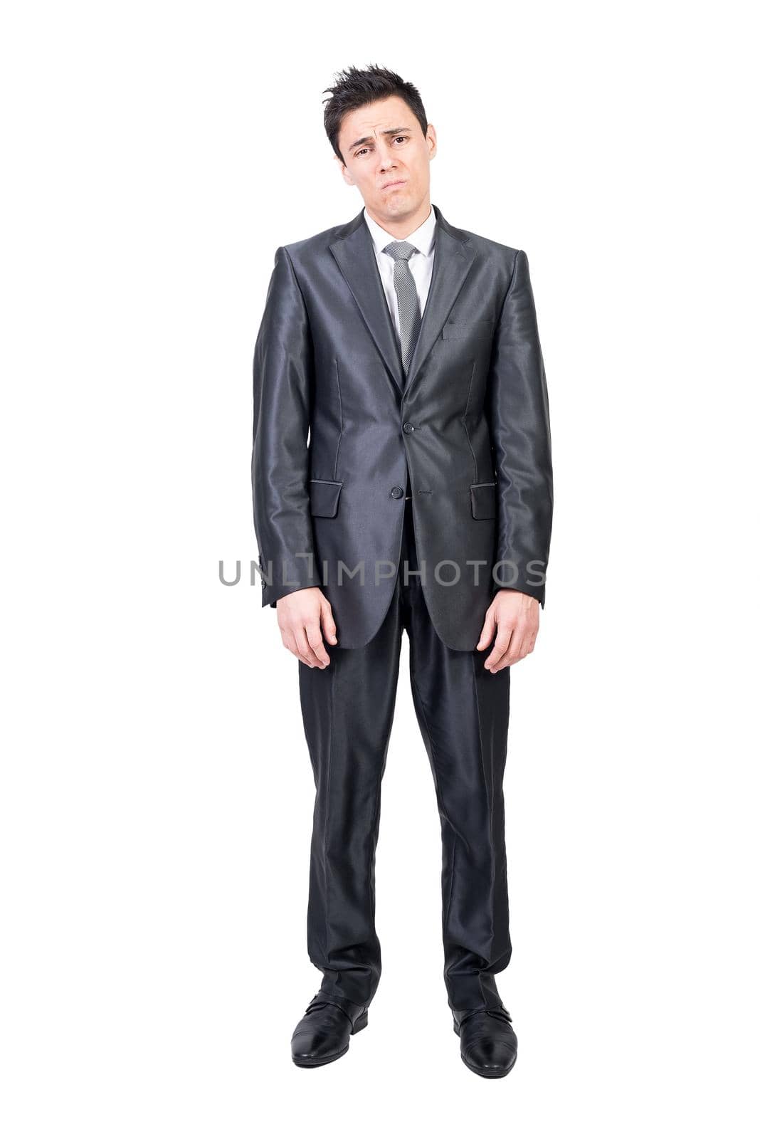 Full length of bored young male employee with dark hair in elegant suit and tie looking at camera with disappointment against white background