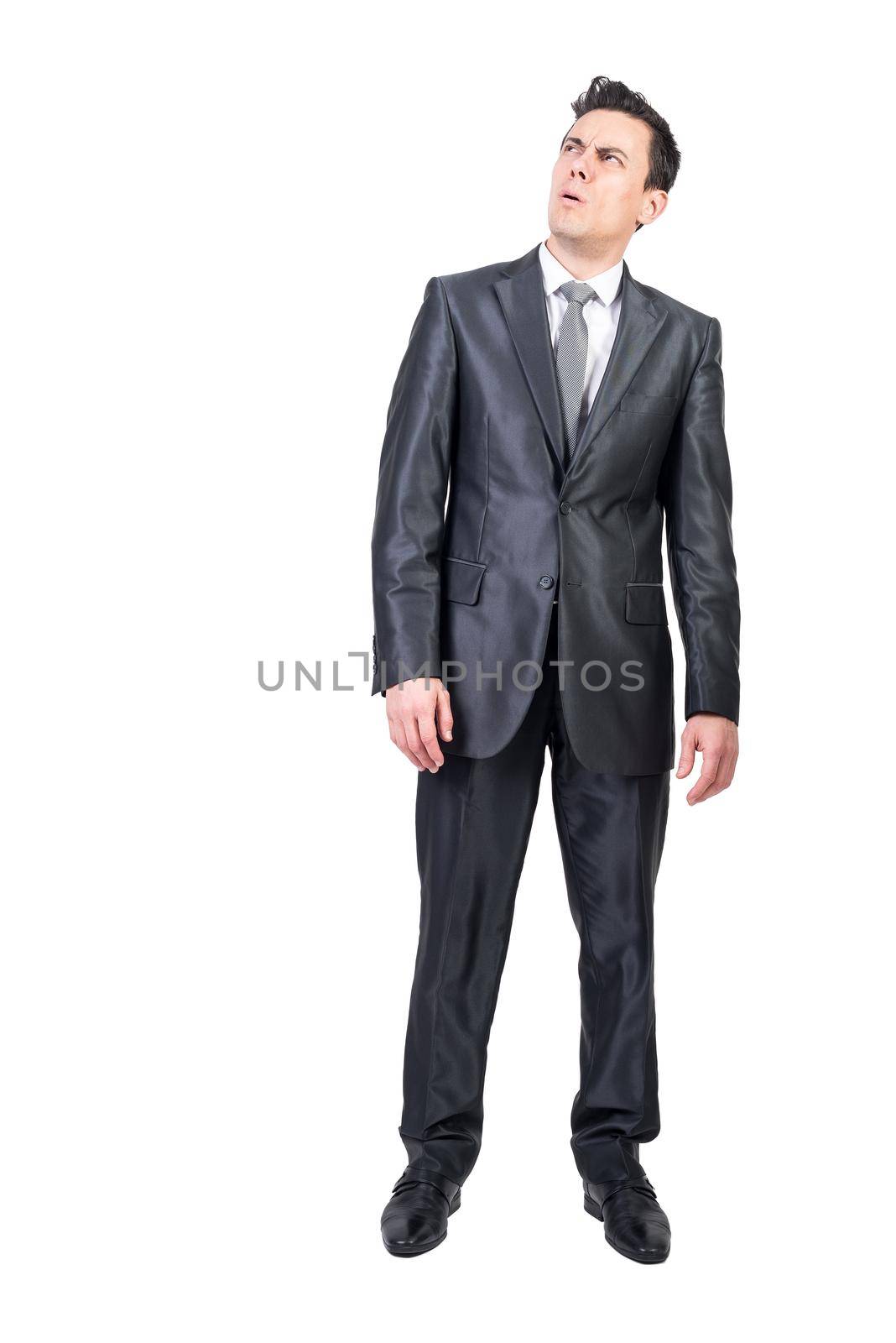 Full body of skeptic male entrepreneur grimacing and looking up while expressing mistrust on white background in studio