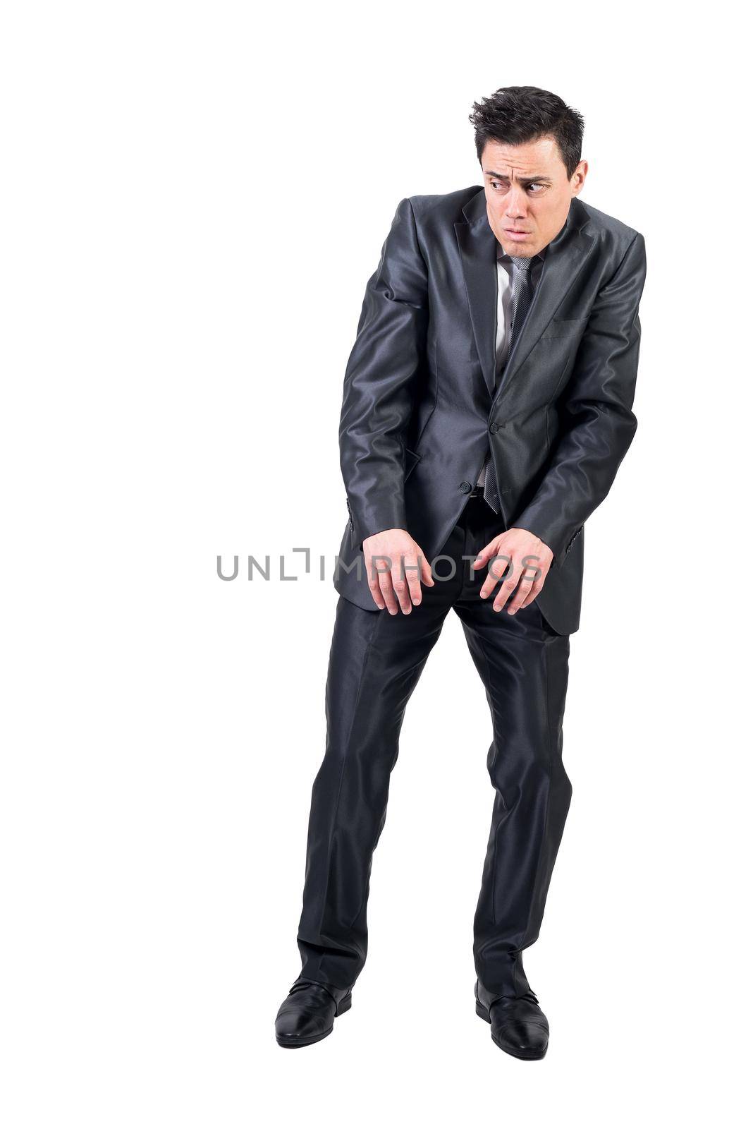 Full body of scared man in elegant formal suit standing isolated on white background with raised shoulders in light studio