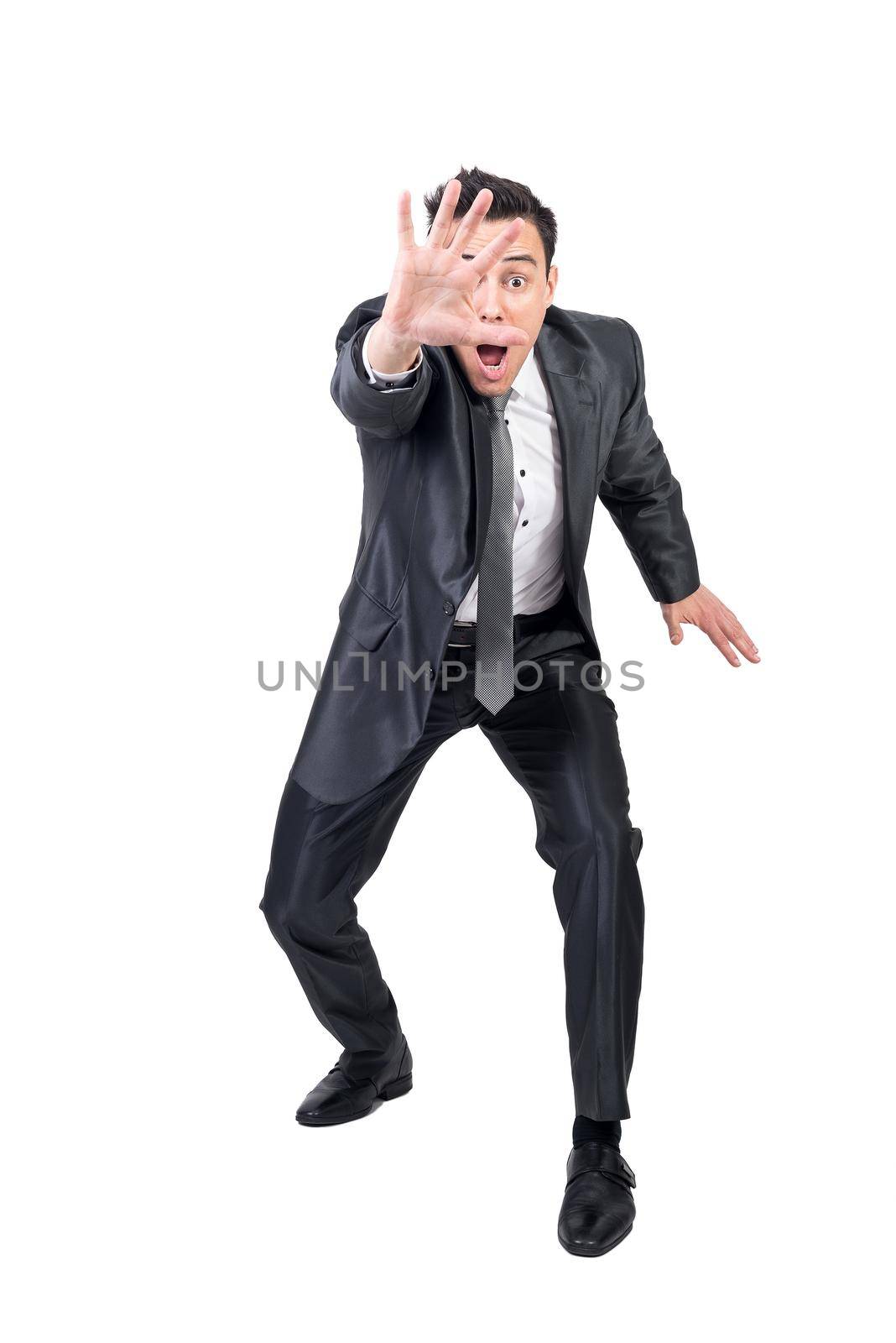 Full body of comic male entrepreneur in classy suit showing stop sign and looking at camera on white background