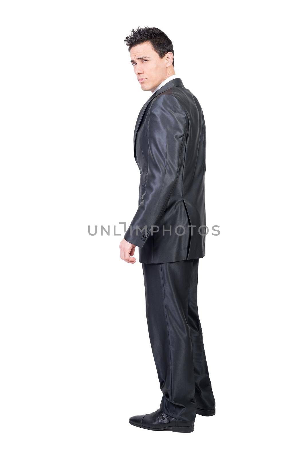 Side view full body of seductive male entrepreneur in classy suit standing in studio against white background and looking at camera