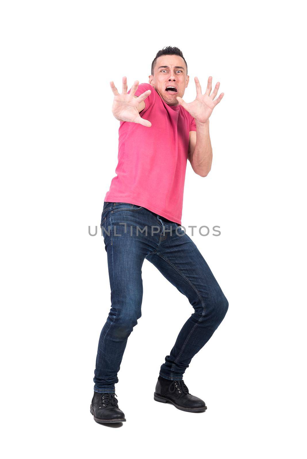 Terrified male in jeans and pink t shirt making protective gesture and shouting in panic while looking at camera and staggering back isolated on white background