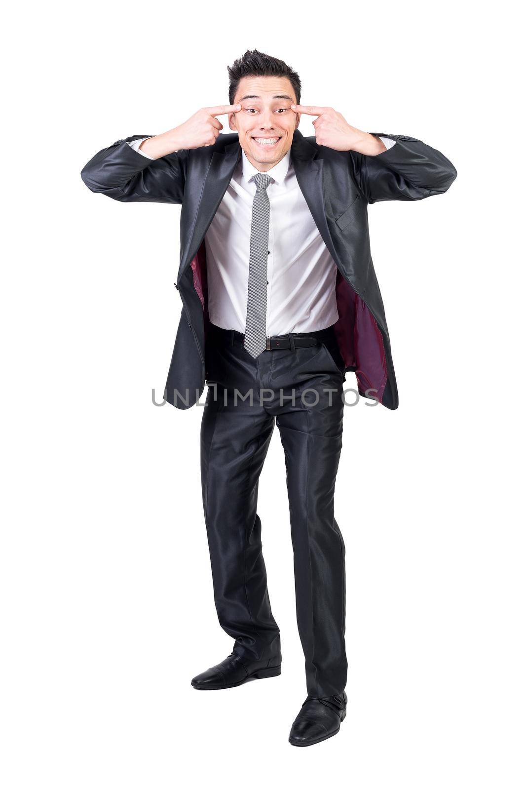 Full body of hilarious male entrepreneur in suit pretending being Asian and showing narrow eyes sign while having fun against white isolated background