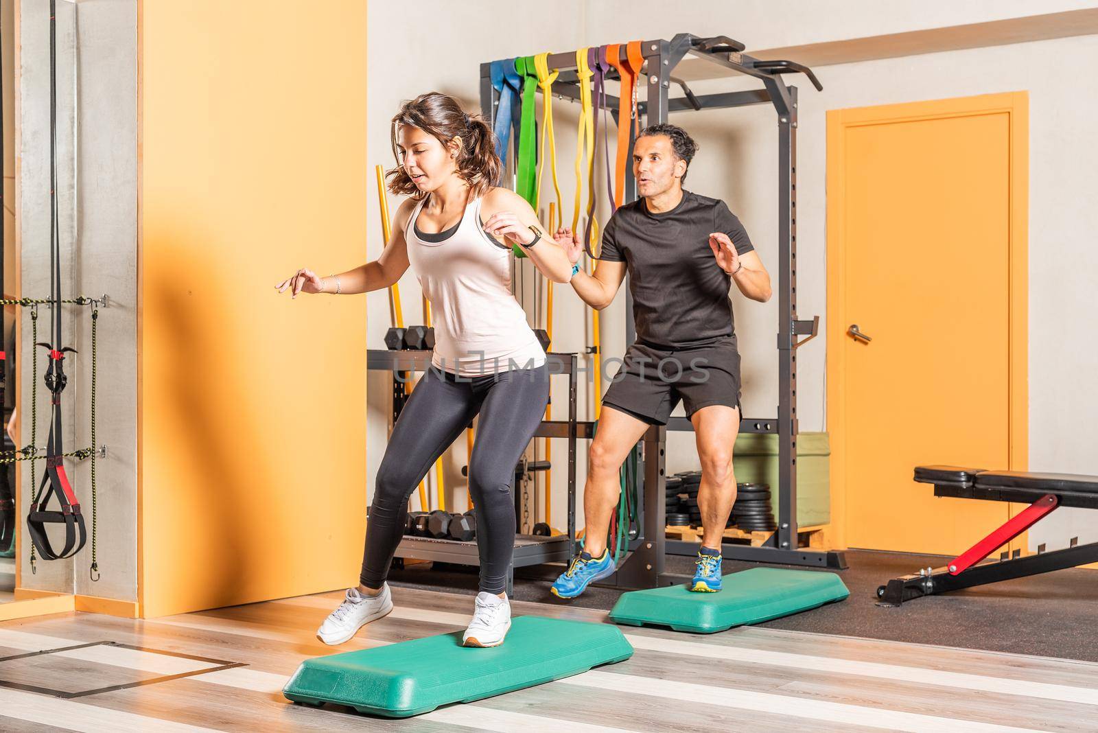 Sportswoman and man doing lateral step up jumps in health club. Concept of exercises with equipment in health club.