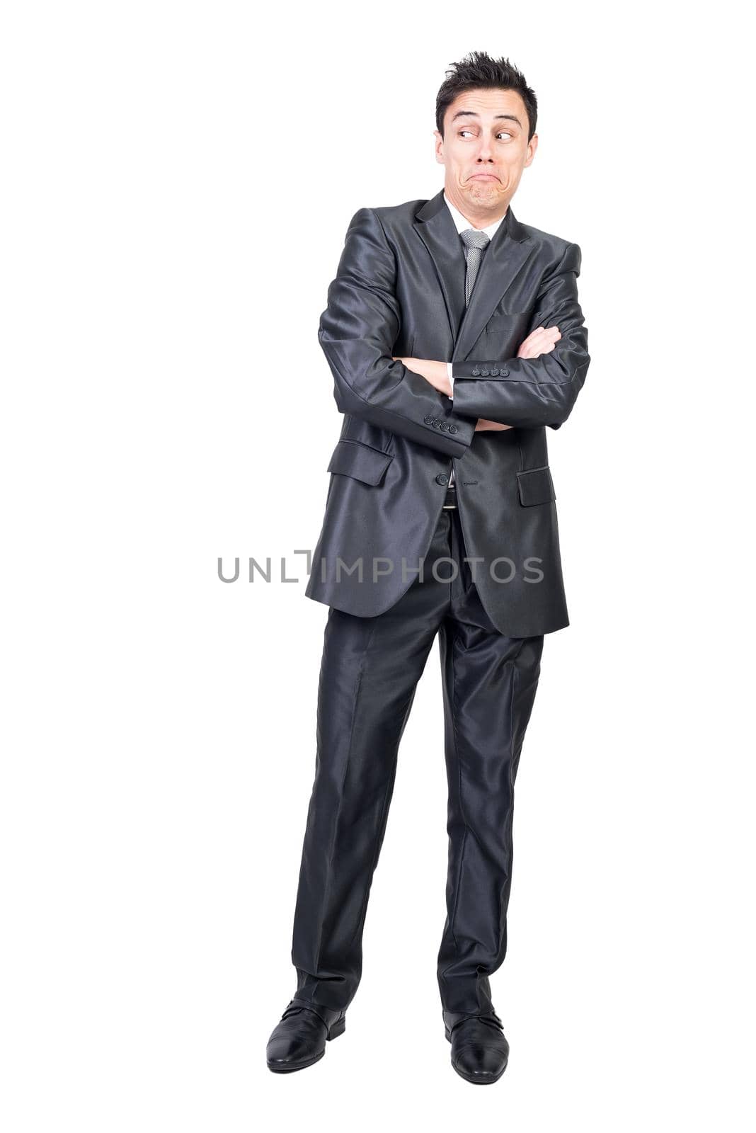 Full body of surprised young male employee with dark hair in elegant suit standing against white background with crossed arms and looking away with doubt