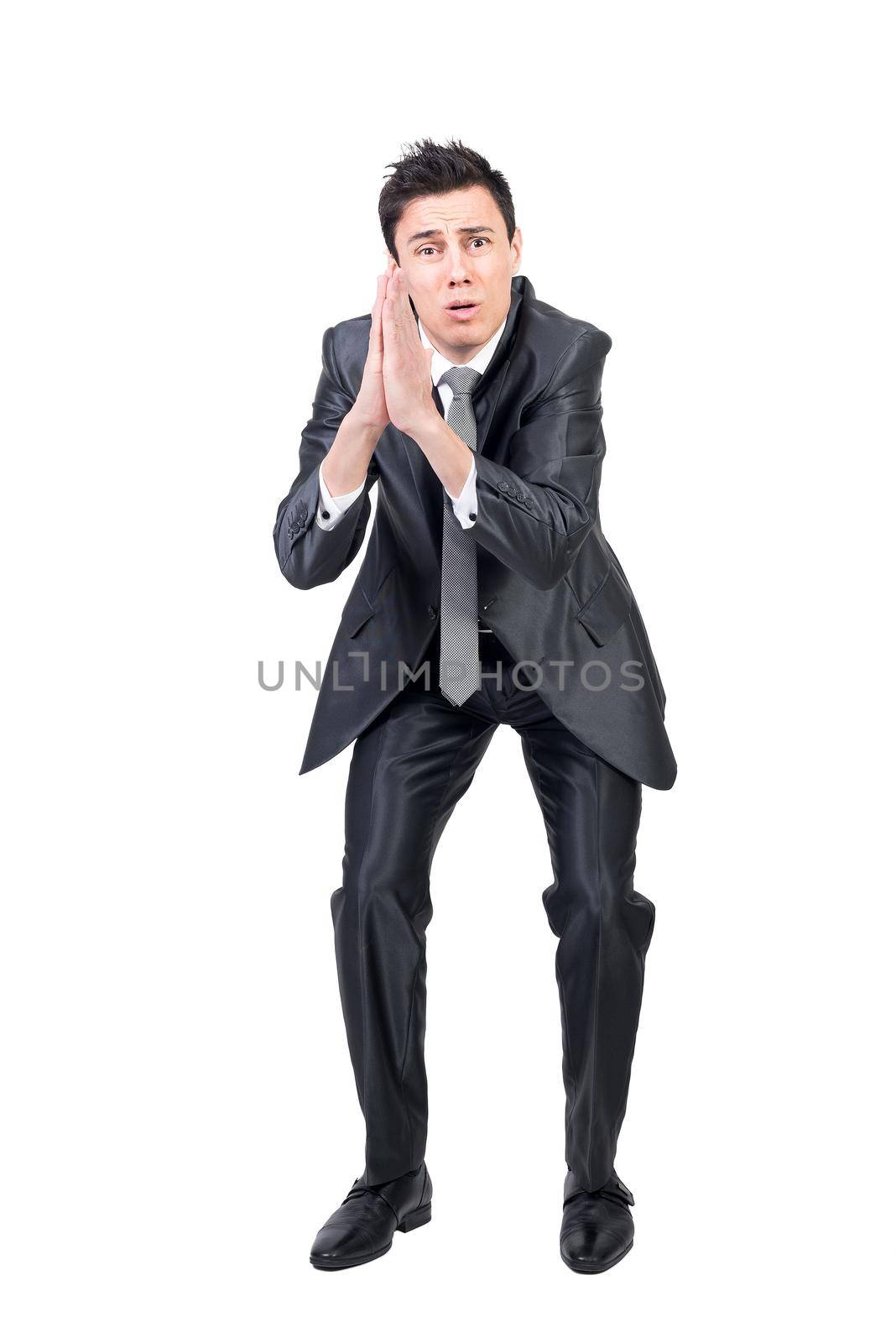 Full body of desperate male model in formal suit keeping has together frowning and asking favor in studio against white background
