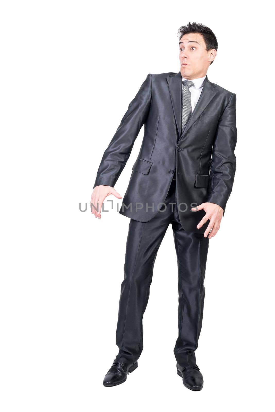 Full length of surprised young male entrepreneur with dark hair in formal suit and tie looking away with astonished face while standing isolated on white background
